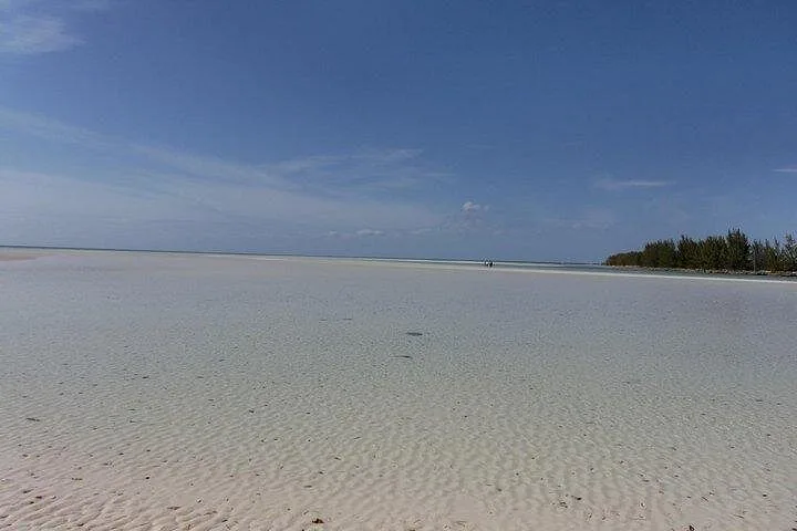 Expansive white sand beach with shallow water and people in distance.