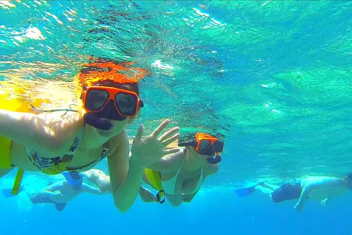 People snorkeling in clear turquoise water, waving at the camera.