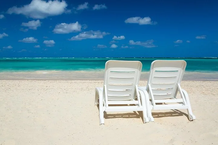 Two white plastic lounge chairs on a white sand beach.